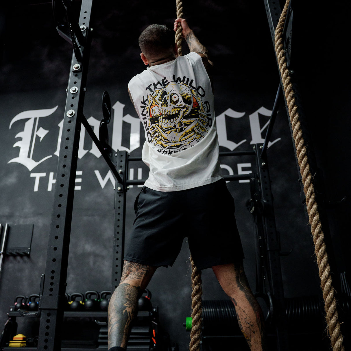 Male model rope climbing in gym wearing the sleeveless street tee with 'Drink The Wild Air' graphic