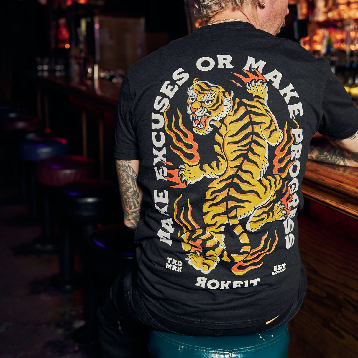 Male model in bar wearing black Active Tee with 'Make Excuses or Make Progress' graphic