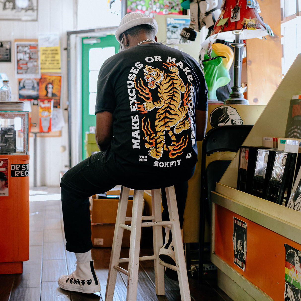 Male model in record store wearing unisex Active Tee with 'Make Excuses or Make Progress' graphic