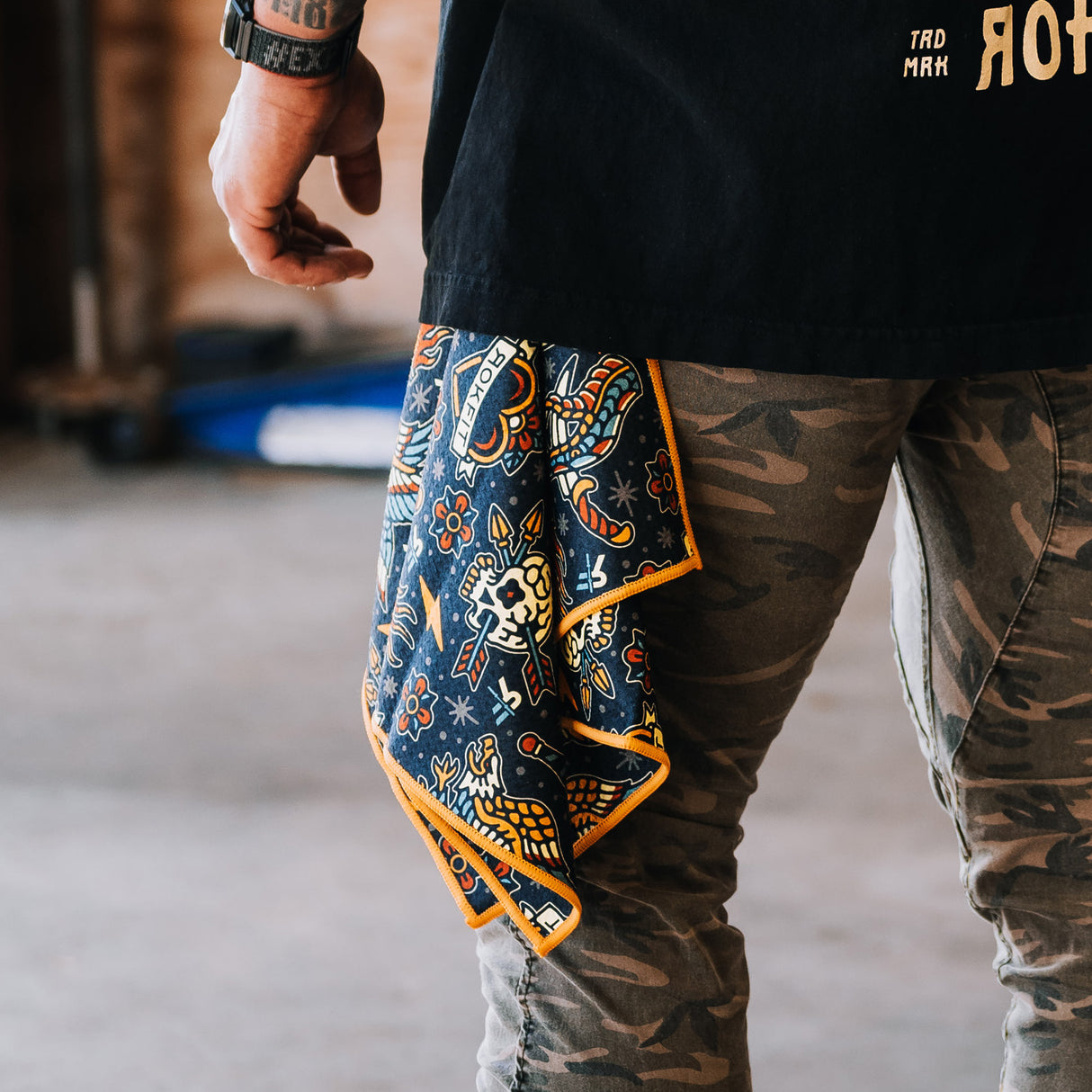 Male model outdoors showing Utility Towel clipped onto belt loop with 'Tattoo Flash Pattern' graphic