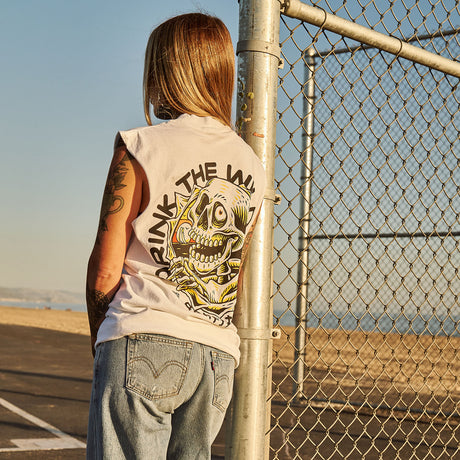 Female model outdoors wearing a sleeveless street tee with 'Drink The Wild Air' graphic