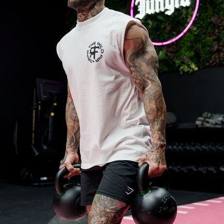 Male model carrying kettlebells in a gym wearing the sleeveless street tee with 'Drink The Wild Air' graphic