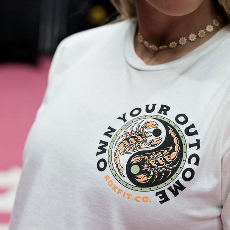 Female model in a gym wearing white crop top with 'Excuses or Reasons' graphic